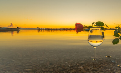 Wall Mural - Verre à vin avec une rose rouge et avec reflets d'un coucher de soleil sur la mer.