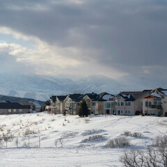 Canvas Print - Square Homes on snowy terrain ovelooking Wasatch Mountain peak and dark overcast sky