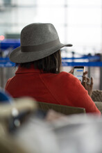 Close Up Portrait Of An Anonymous Afro American Lady Silhouette With A Fancy Hat And A Red Jacket, Waiting In An Airport Lounge With Her Phone, Roissy Charles De Gaulle, Paris Airport, France, Europe.