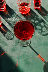 Creative beverage photography of red cocktail in different glasses under hard light over green background.