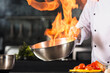 © stockbusters - Chef hands hold wok with fire. Closeup chef hands prepare food with fire.