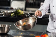 © stockbusters - Chef hand keep wok. Closeup hands tossing food at professional kitchen.