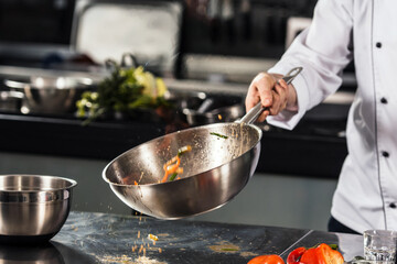 Chef hand keep wok. Closeup hands tossing food at professional kitchen.