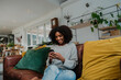 © Prins Productions - Young mixed race woman with afro chatting on smart phone on the sofa at home