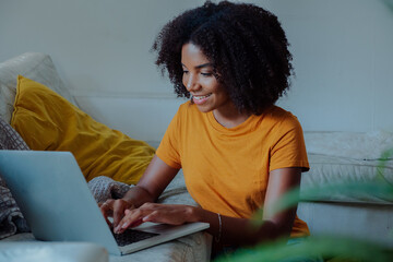 Beautiful young woman typing on laptop, happy freelancer working from home on the sofa