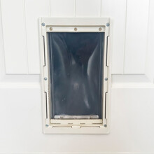 Square Close Up Of Pet Door Or Pet Flap Against White Wooden Panelled Door Of Home