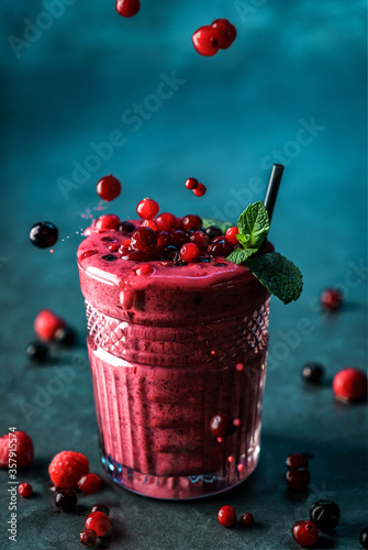 Fresh smoothie currant, raspberries and mint in glass on dark blue background. Studio shot of drink in freeze motion, berries in flying. Summer cold drink and healthy breakfast