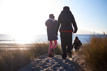 A Family Walks Toward The Sea Through Sand Dunes On A Bright Sunny Day In Winter