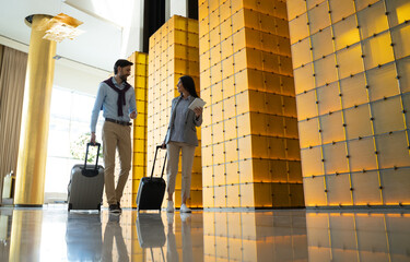 Elegant couple travelling on business, dragging their suitcases by a hotel hall