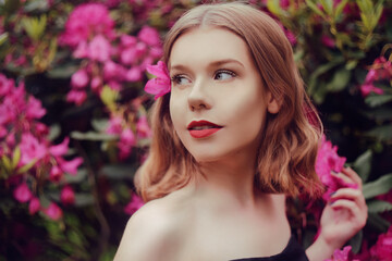 Portrait of a gorgeous girl with hair in flowers, a blonde against a back of pink flowers, a summer photo in a fashionable tint. Beautiful in a fairy garden in beautiful makeup with a short haircut