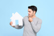 © Atstock Productions - Young man looking at house model and thinking isolated on light blue background
