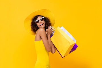 Happy surprised woman with colorful shopping bags smiling on yellow background for summer sale concept