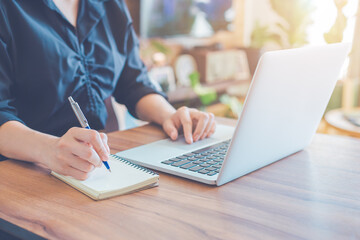 Wall Mural - Business woman is writing on a notebook with a pen and using a laptop to work in the office.