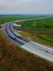 The two trucks driving on the highway winding through rice fields landscape