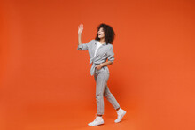 Joyful Young African American Woman Girl In Gray Casual Clothes Posing Isolated On Orange Background. People Lifestyle Concept. Mock Up Copy Space. Waving And Greeting With Hand As Notices Someone.
