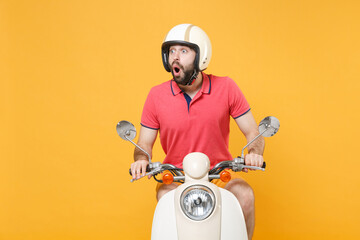 Shocked young bearded man guy in casual summer clothes helmet driving moped isolated on yellow background studio portrait. Driving motorbike transportation concept. Mock up copy space. Looking aside.