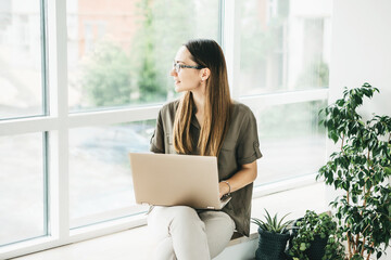 Beautiful young adult girl is using a computer. She is distracted and looks out the window or she is dreaming.