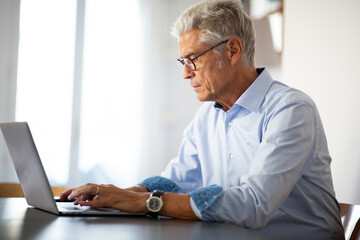 Wall Mural - Side of businessman with glasses sitting at office desk using laptop comp[uter