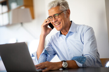 Close up smiling businessman talking with phone while looking at laptop computer