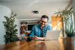 © bnenin - Portrait of a handsome smiling man writing in note pad and using laptop, at home.