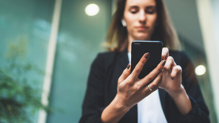 Wall Mural - front view of a businesswoman holding a smartphone while sending messages. Confident female employee using a mobile app for online banking on a mobile device, standing next to office