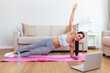 © Graphicroyalty - ortrait of young attractive woman doing exercises while watching online lessons on her laptop. Healthy lifestyle and sports concept. Shot of fitness woman sitting on exercise mat
