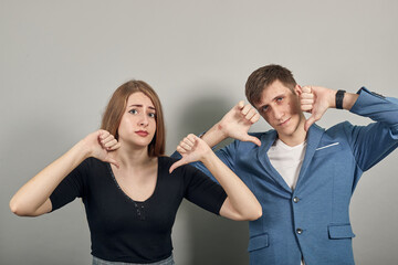 Human hand thumb down, no okay sign, angry face, negative gesture showing dislike with finger, rejection. Young attractive couple boyfriend girlfriend two people, dressed black t-shirt, blue jacket