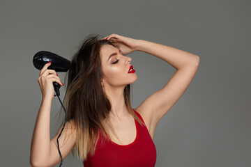 Wall Mural - Beautiful young woman drying her hair with dryer on gray background