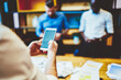 © BullRun - Selective focus on male hands typing text in app on smartphone with blank copy space area. Cropped view of cellular, business person using mobile phone while office colleagues on standing background