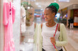 © TheVisualsYouNeed - young beautiful and happy afro American girl at buying shopping mall - lifestyle portrait of millennial black girl enjoying looking  clothing at beauty fashion store