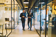 © BullRun - Adult dedicated multiracial business partners having interesting conversation while walking along light office corridor