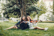 © hetmanstock2 - Girls in a summer park. Two ladies with a violin. Friends sitting on a grass