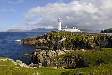 Magnifique phare blanc posé sur des falaises rocheuses et verdoyantes au bord de la mer bleu indigo de l'Irlande du nord.