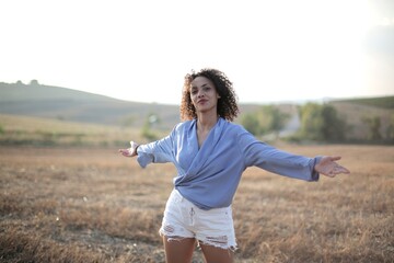 Wall Mural - Curly-haired female with open hands standing on a field