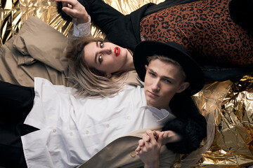 Stylish couple posing on a golden background from a foil lying.