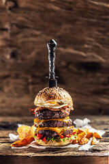 Canvas Print - Knife stabbed in a triple cheeseburger with beef patty, melted cheese, egg and peppers in a rustic wooden environment