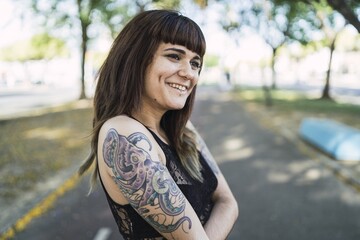 Sticker - Young attractive Caucasian female with tattoos standing in the park making a cute face