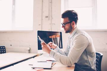 Poster - Concentrated male IT developer making setting in new application on mobile updating software, young man in eyewear texting message chatting in networks on smartphone during work break in office