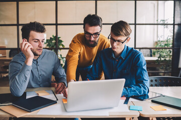 Poster - Group of young male coworkers watching webinar online via online application on modern laptop computer, serious skilled men making research for startup project browsing internet on netbook device