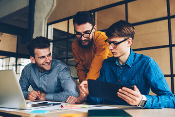 Happy male colleagues having fun during working process collaborating in friendly atmosphere, cheerful programmers satisfied with completing successful project together using modern technology