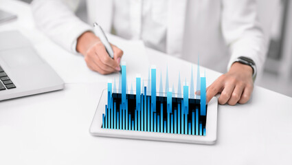 Poster - Business woman writing something at her desk and financial graphs rising from tablet screen, collage
