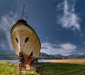 Wall Mural - old big ship against the blue sky stands on the shore on props, the shore of the lake in the mountains,