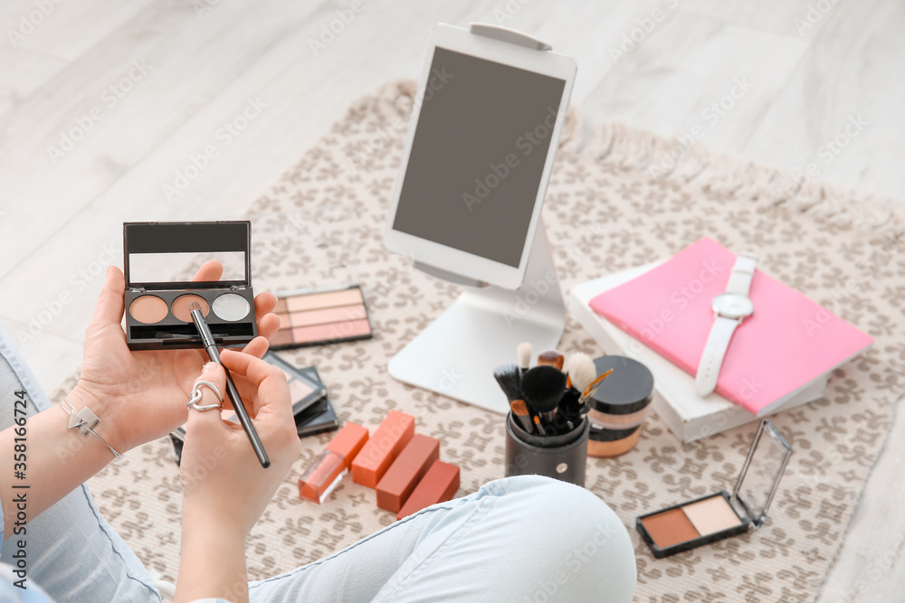 Makeup artist with modern tablet computer and decorative cosmetics sitting on floor