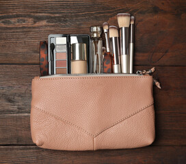 Cosmetic bag with makeup products and beauty accessories on wooden background, flat lay