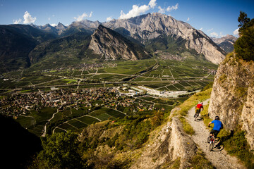 riddes, switzerland. two men ride mountain bikes along a narrow exposed trail in the swiss alps. the