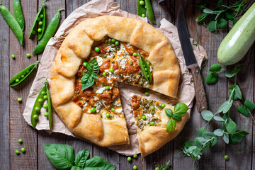 Vegetarian Open pie with green peas and zucchini on wooden table. top view.