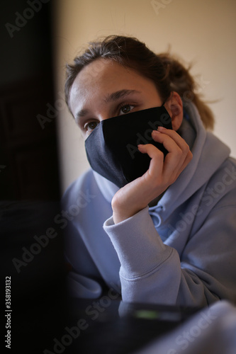 Fotomural Girl in a black mask works on a laptop at home in isolation