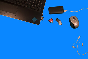 Sd card battery supply cords lap top and mouse flat lay on a blue desk top. showing personal data storage gadgets with open space for customer product placement.