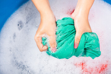 Wall Mural - Closeup young Asian woman use hands washing color clothes in basin. Female squeeze wring out wet fabric cloth with detergent have soapy bubble in water, studio shot background, laundry concept