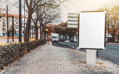 Blank white advert billboard template on a paving stone near the road; empty ad banner placeholder mockup template on the sidewalk; poster mock-up in urban settings with a copy space area on the left